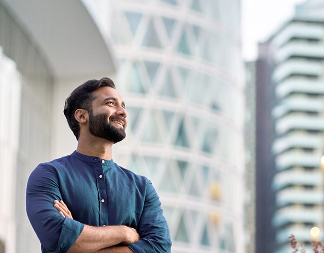 Happy wealthy rich successful indian business man standing in big city modern skyscrapers street on sunset thinking of successful future vision, dreaming of new investment opportunities concept.